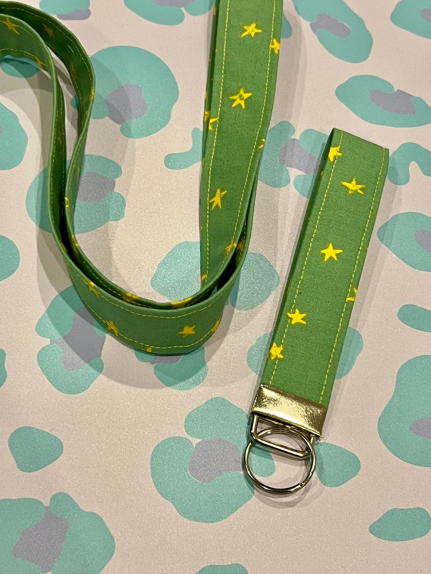 Green lanyard with yellow stars and wristlet keychain on a patterned background