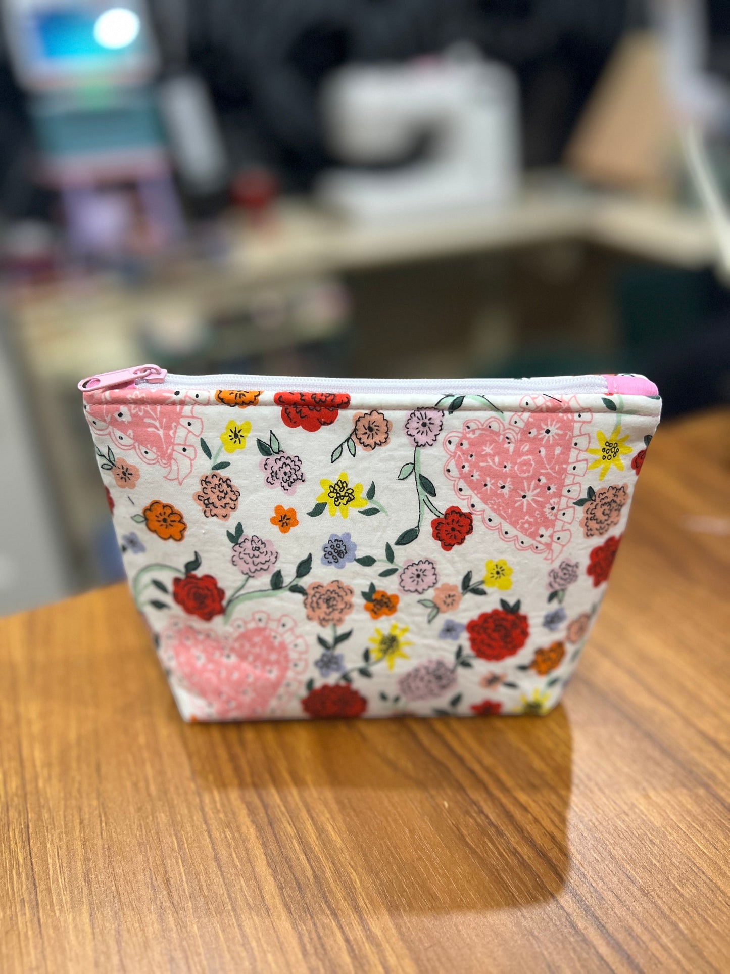 Sew Much Love mini cosmetic bag with white background, pink hearts, and multicoloured floral print. Features a pink zipper pull.
