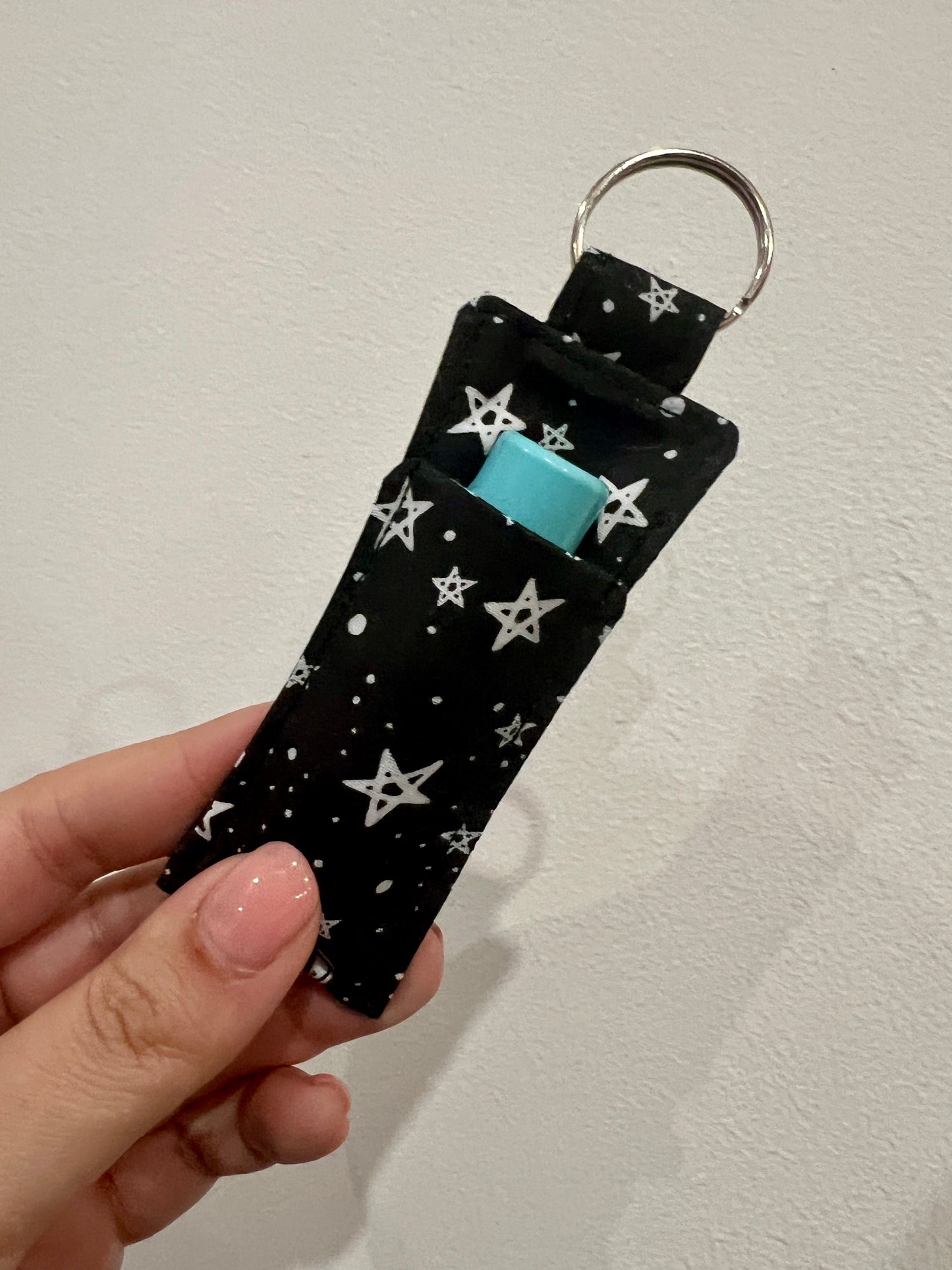 Keychain with star pattern and blue lip balm inside, held by a hand against a neutral background
