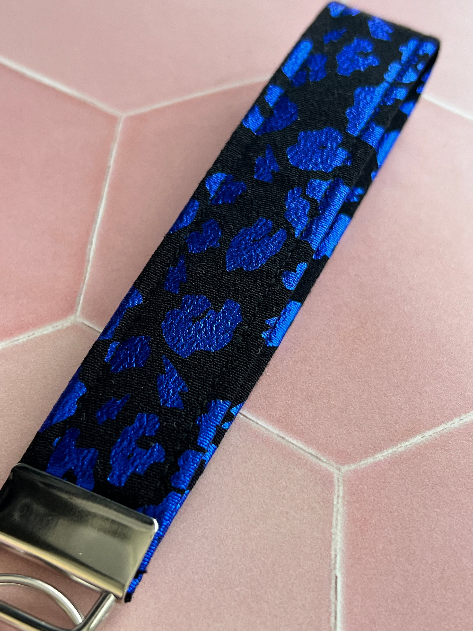 Close-up of black and blue foil leopard print fabric wristlet keychain, showing vibrant shimmer detail and silver keyring attachment