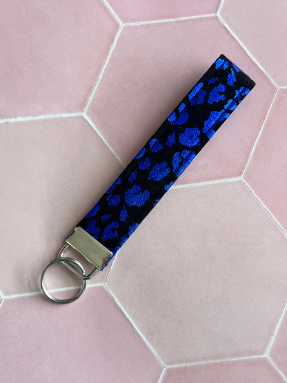 Flat lay of handmade black fabric wristlet keychain with shimmering blue foil leopard print, perfect for carrying keys and small essentials