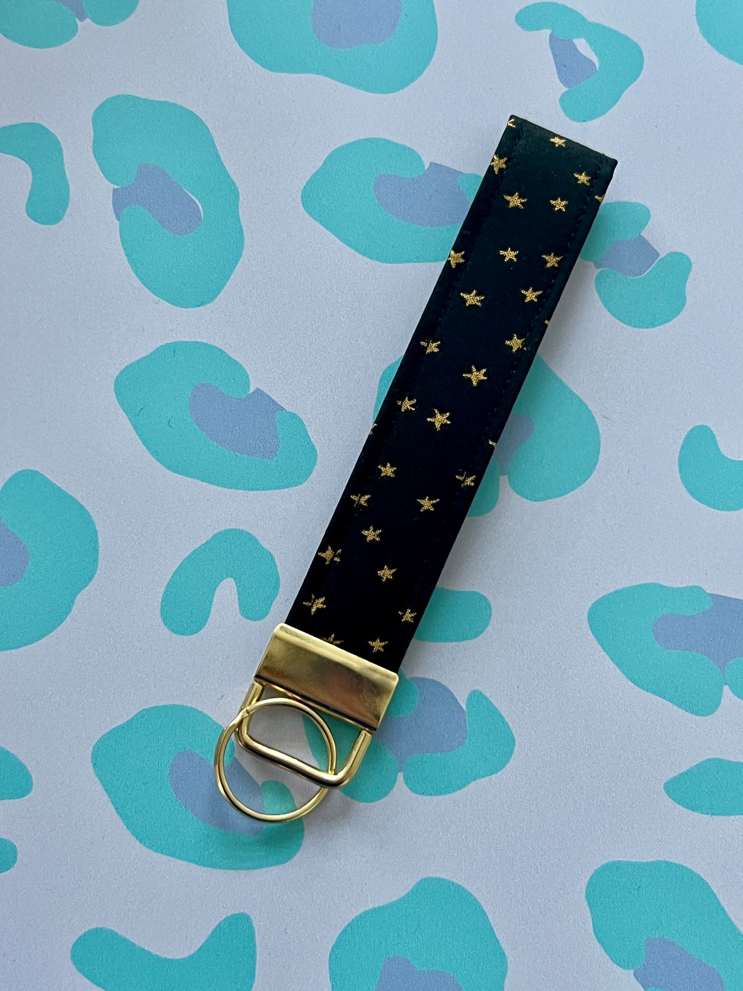 Black keychain with gold stars and a gold ring on a blue and green patterned background