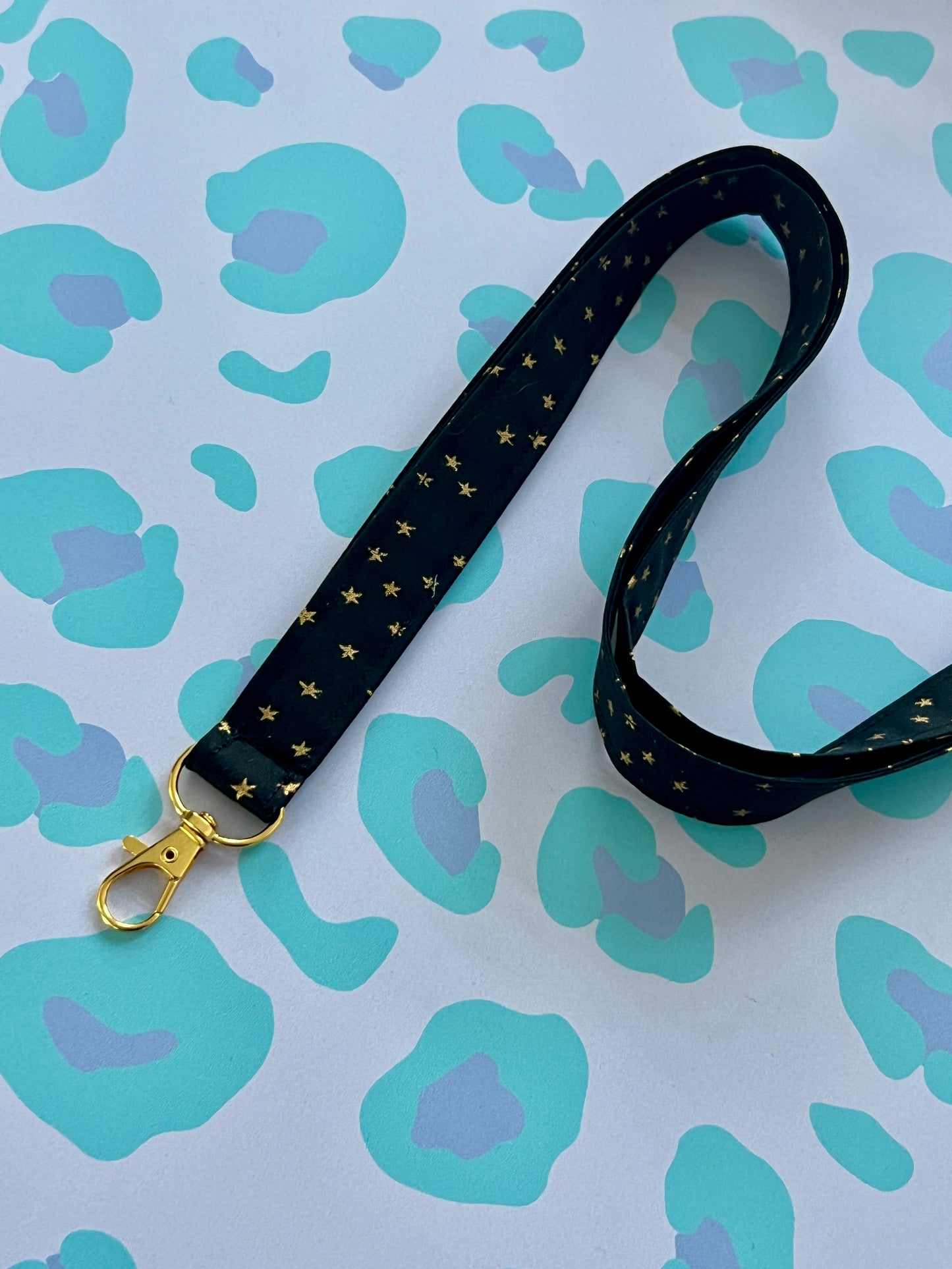 Black lanyard with gold stars on a blue and purple patterned background