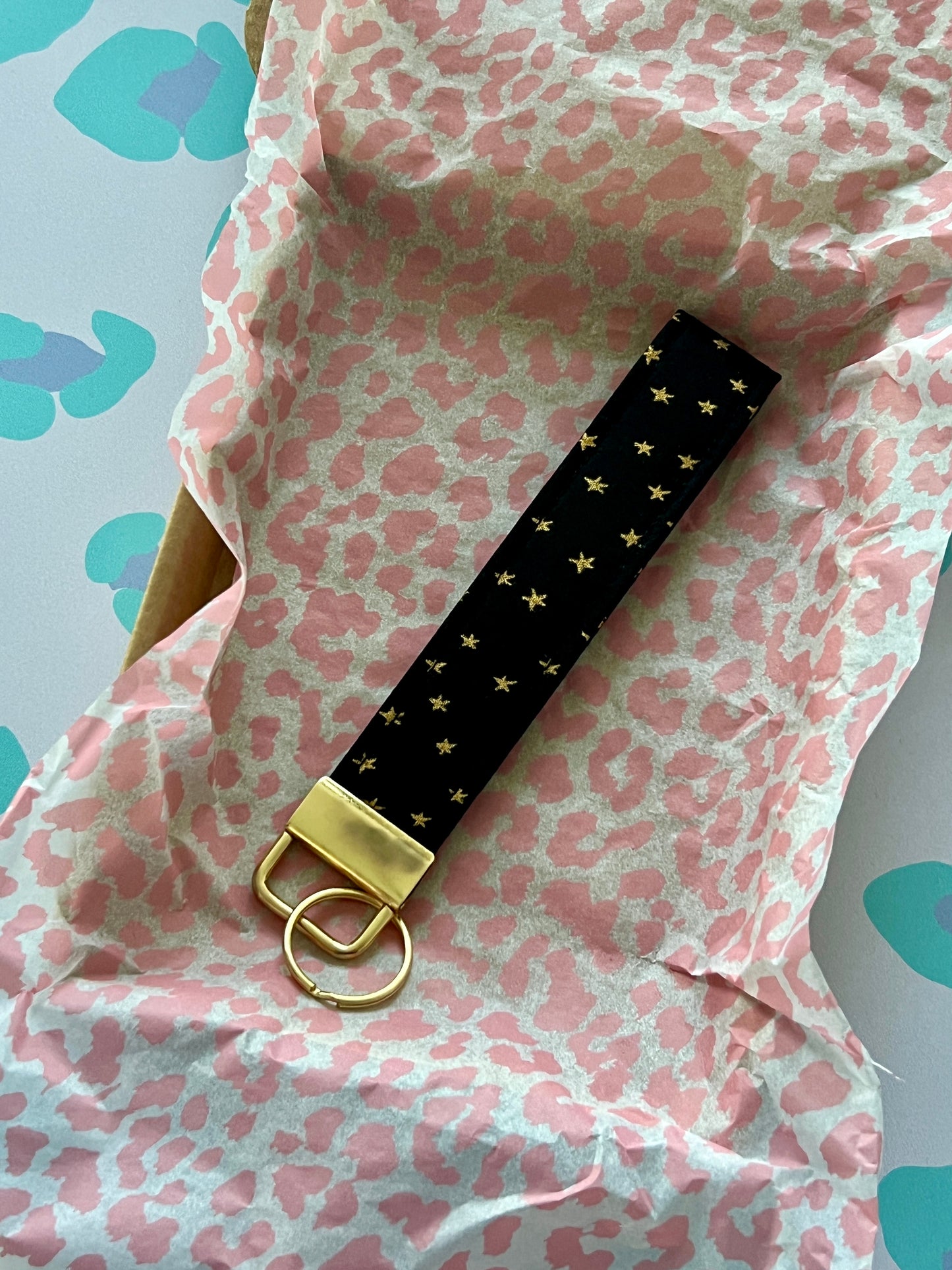 Black keychain with gold accents on pink and white patterned fabric
