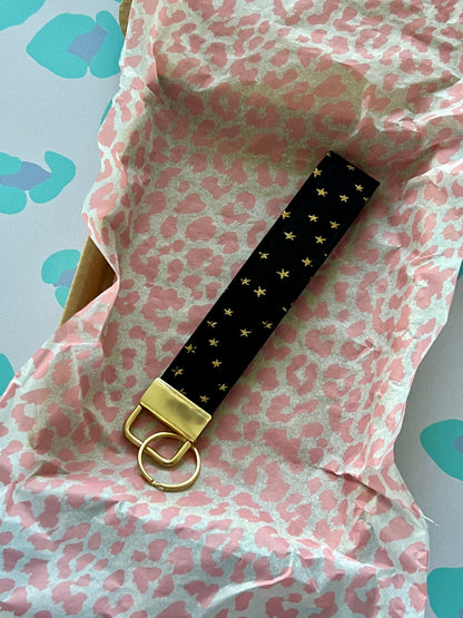 Black keychain with gold accents on pink and white patterned fabric