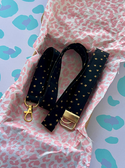 Black strap with gold accents on a pink and blue patterned background