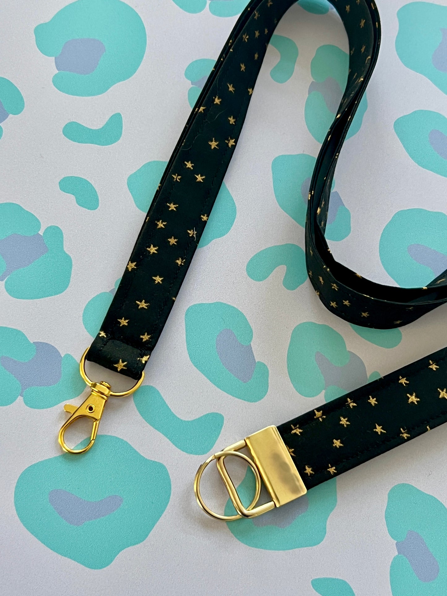 Black lanyard with gold star pattern and clasp on a patterned background