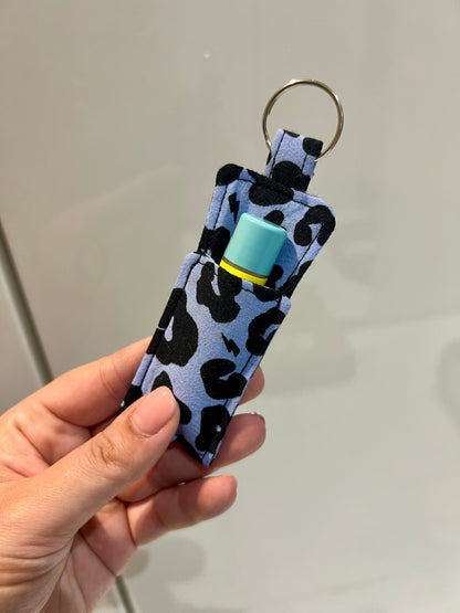 Hand holding a keychain with a leopard print pattern and a small device on a plain background