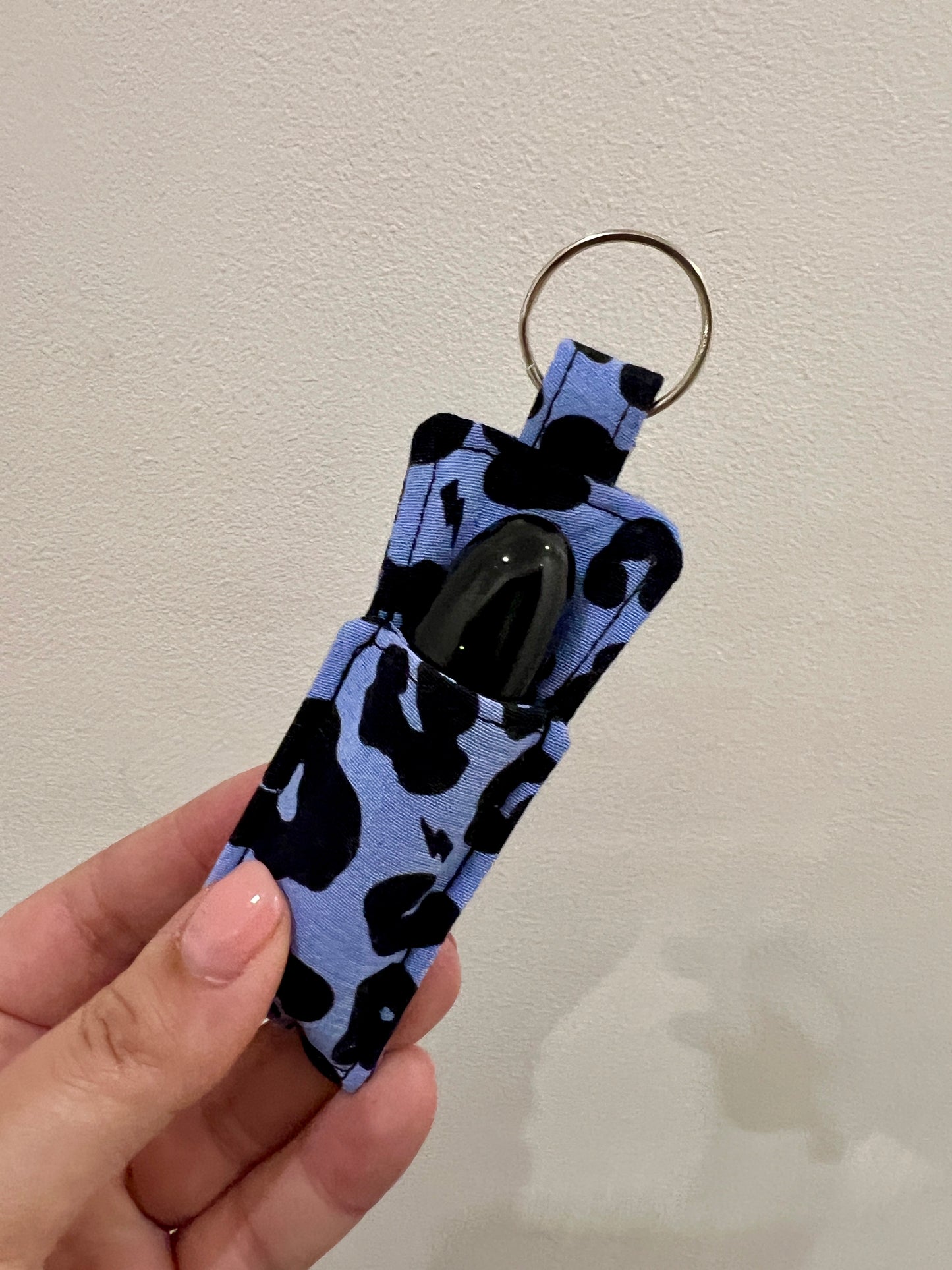 Hand holding a blue keychain with black patterns against a plain background