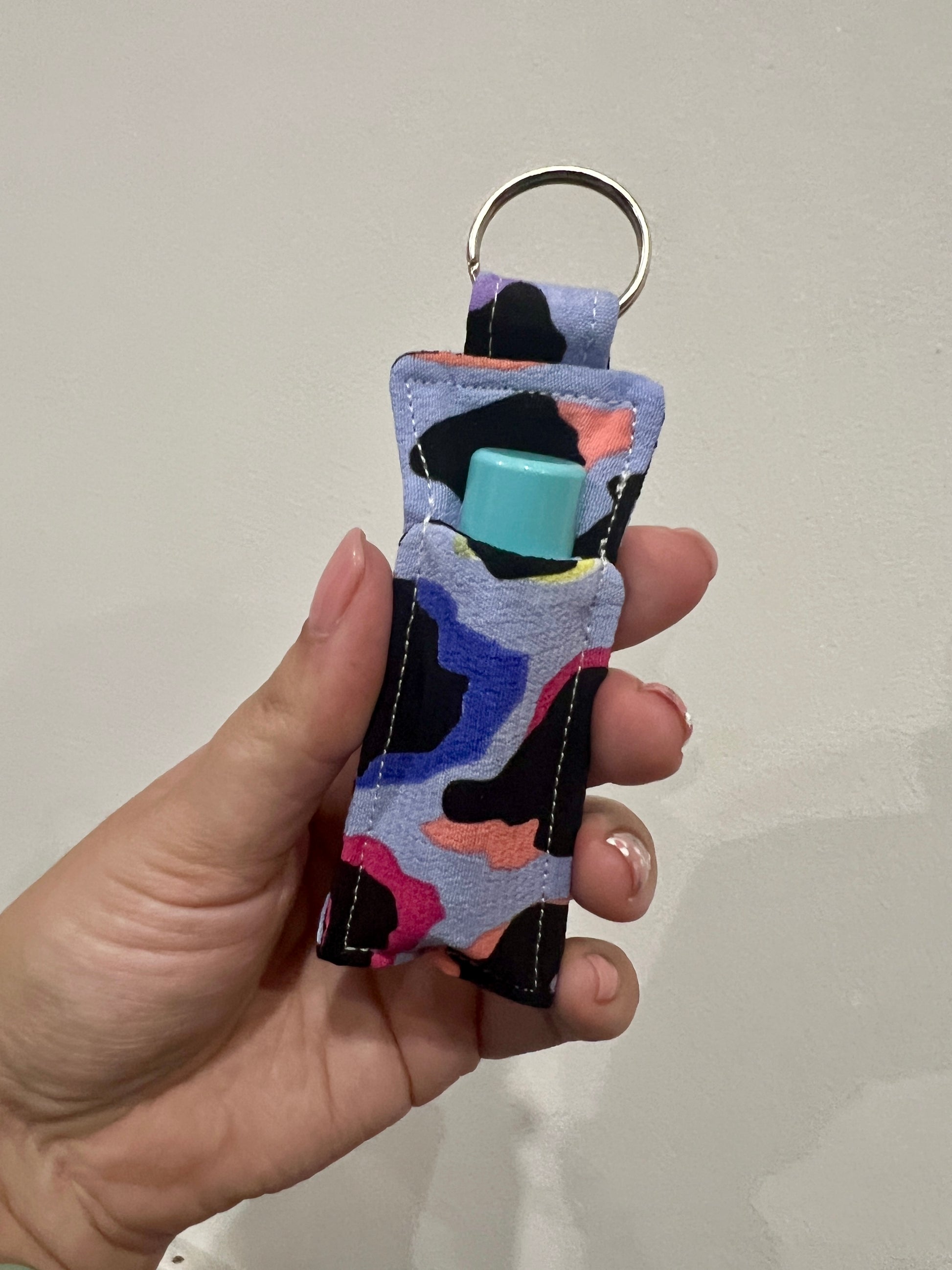Hand holding a colourful lip balm holder keychain with a lip balm on a plain background