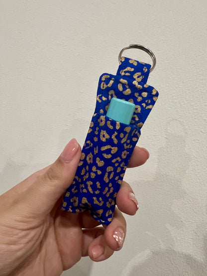 Hand holding a blue keychain with gold leopard print pattern against a plain background