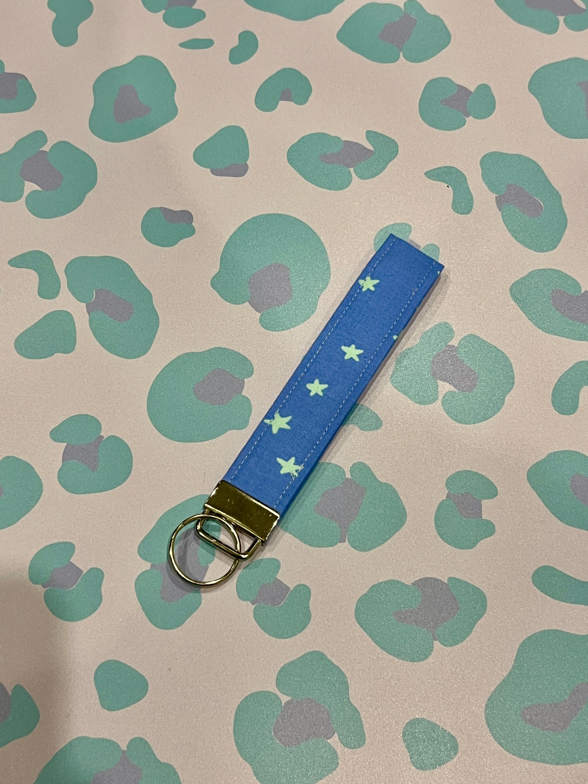 Blue keychain with star pattern on a beige background with green abstract shapes