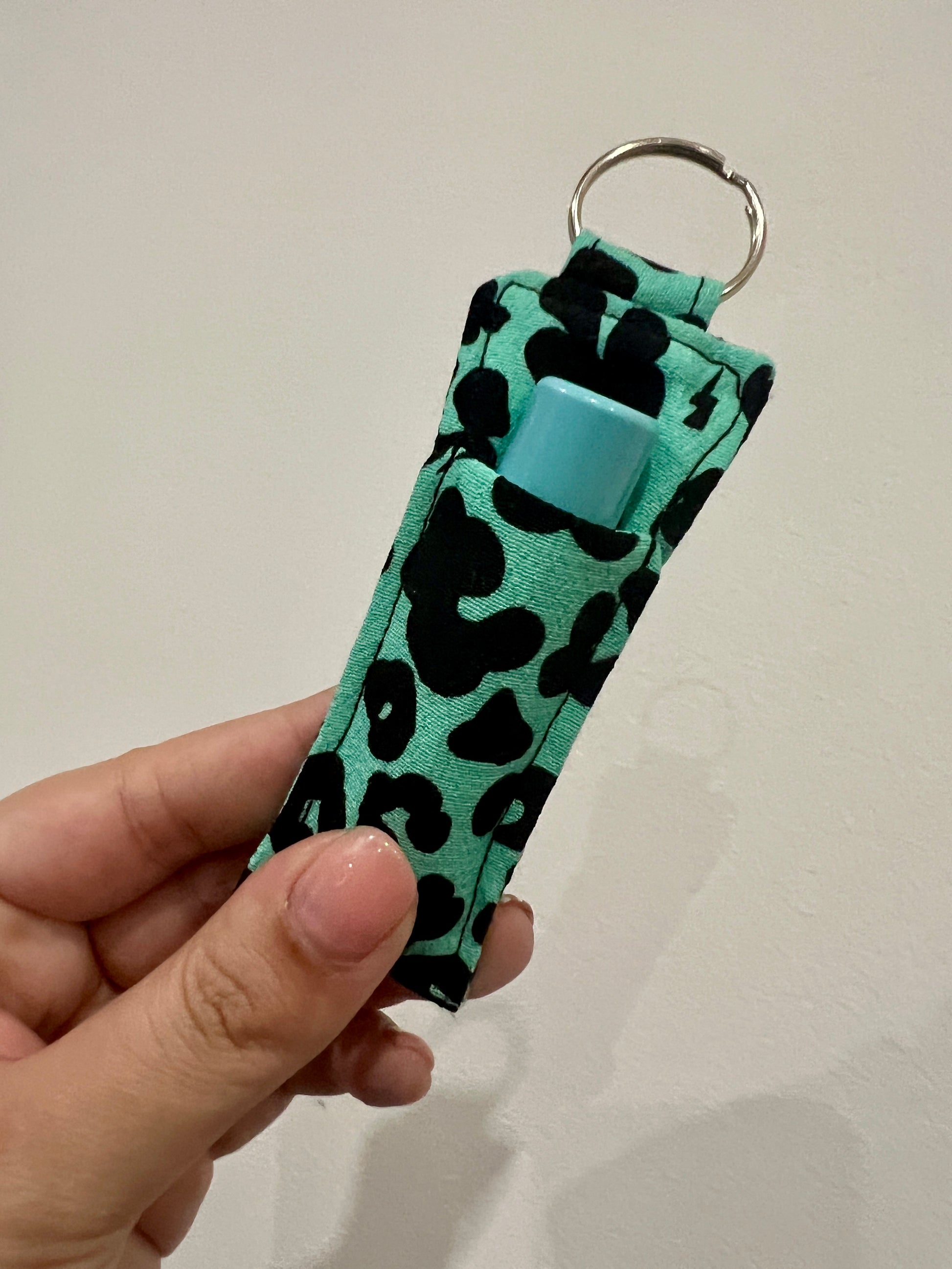 Keychain with leopard print with lip balm held by a hand against a plain background