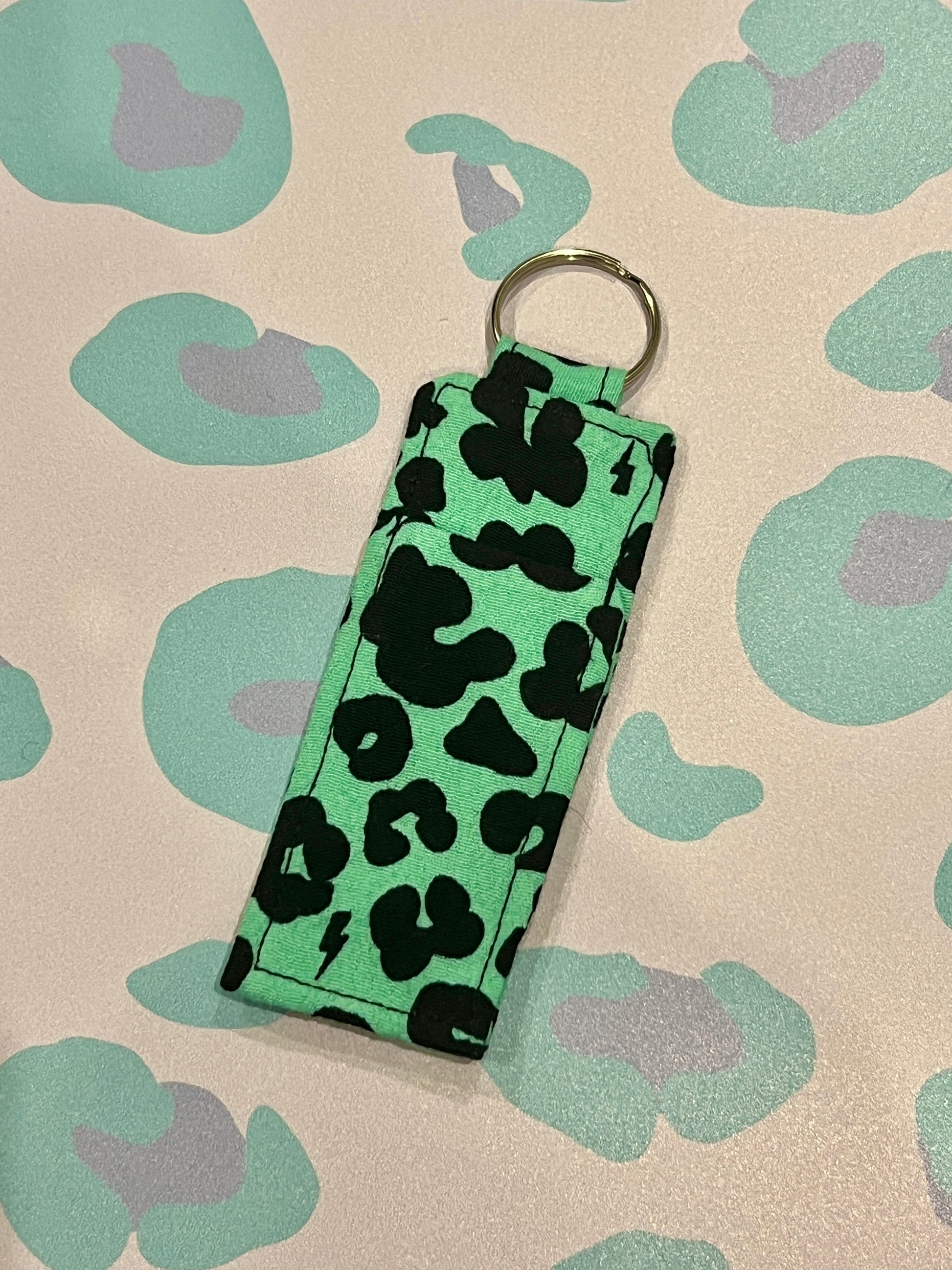 Keychain with green and black pattern on a beige background with green and purple shapes