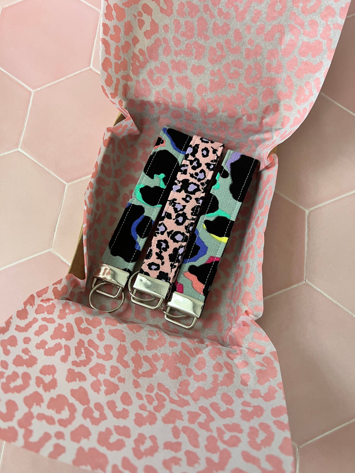 2 Khaki Rainbow Leopard Print Wristlet Keychain with a purple and pink wristlet keychain in a packaging box