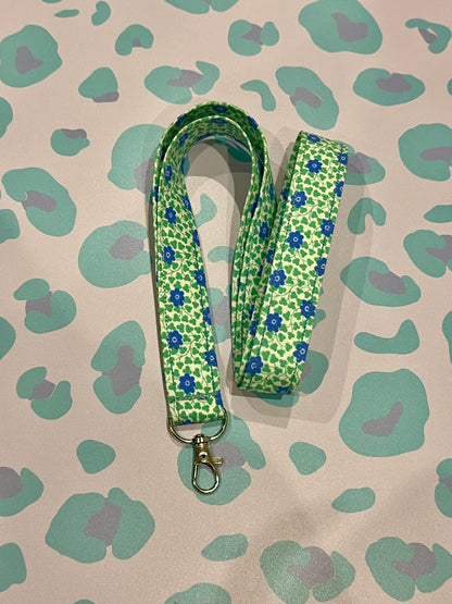 Green floral patterned lanyard on a beige background with green and purple abstract shapes