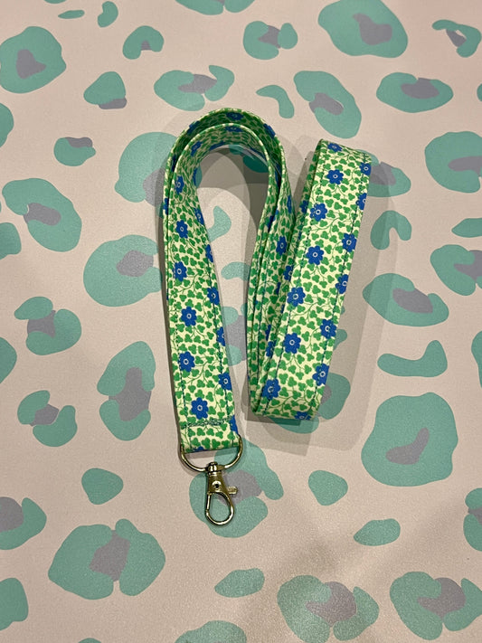 Green floral patterned lanyard on a beige background with green and purple abstract shapes