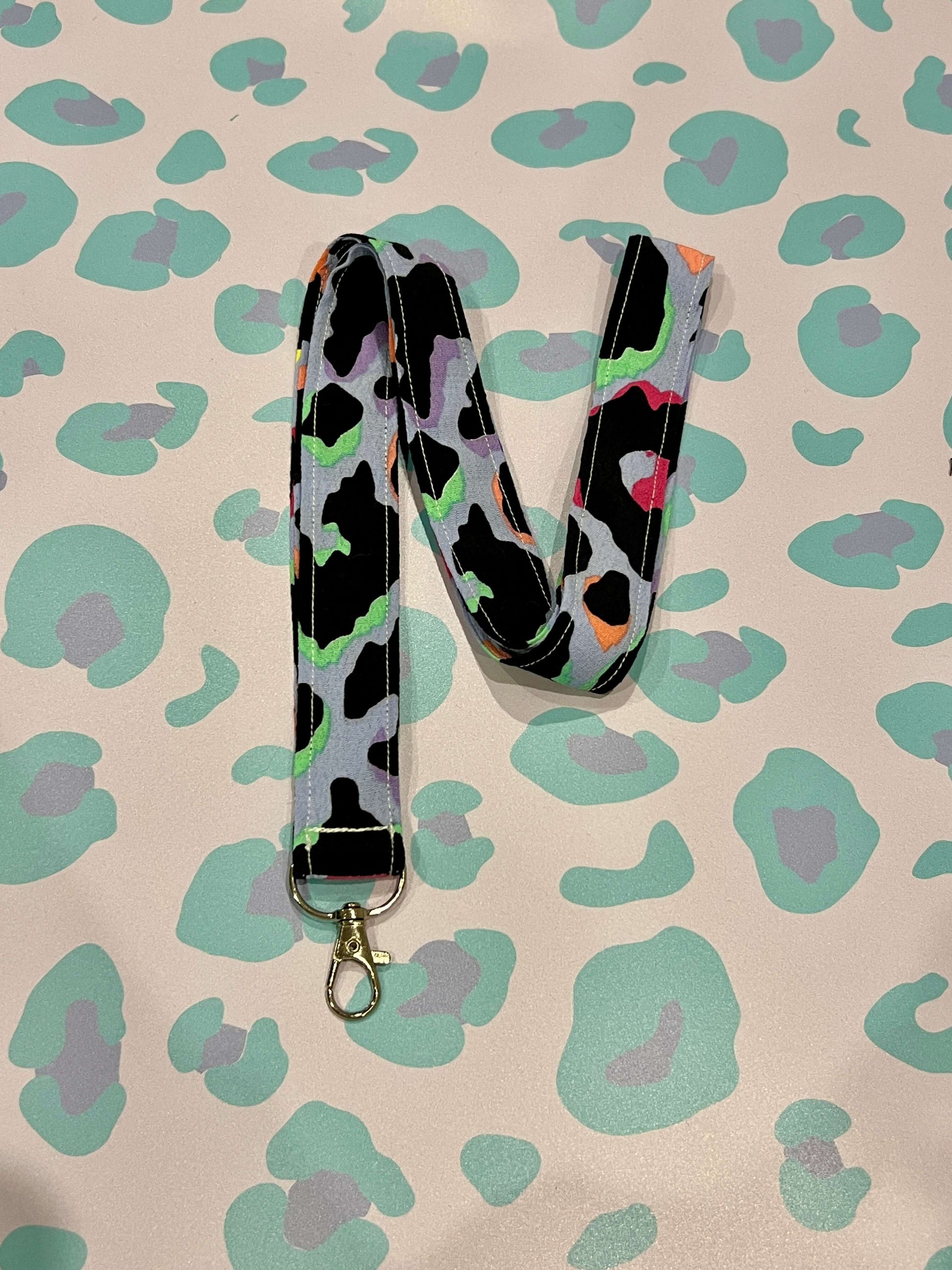 Colourful Light Blue Rainbow Leopard Print Lanyard on a leopard print background with green and purple.