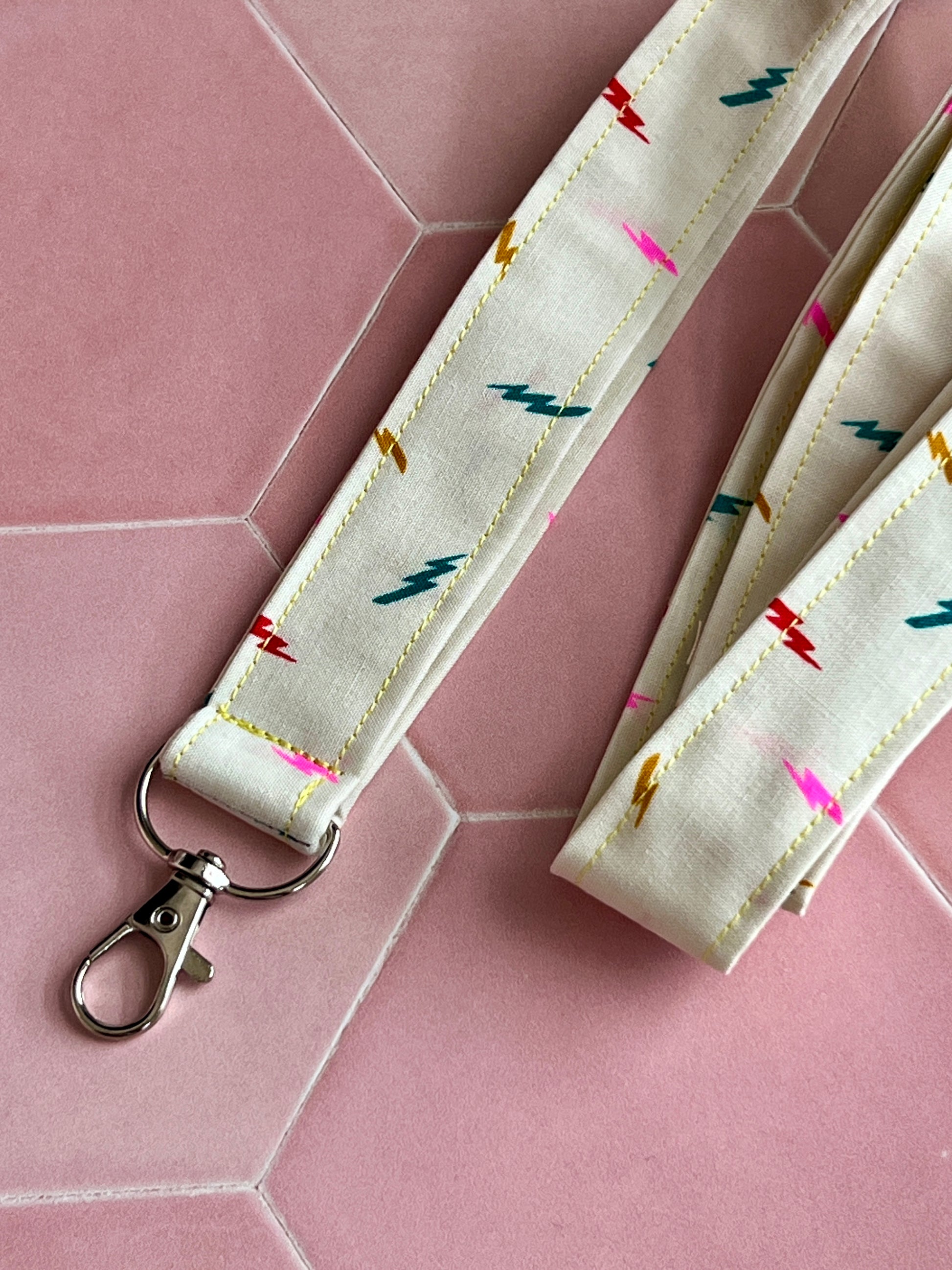 Close-up of handmade lightning bolt lanyard, cream cotton fabric with pink, blue, red, and yellow bolts, D-ring key holder