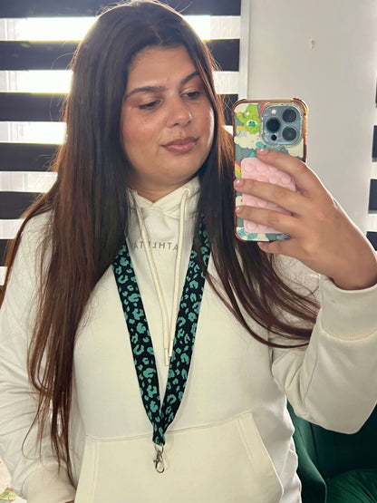 Brand Owner Elana taking a mirror selfie with a phone, wearing a white hoodie and green leopard print lanyard.