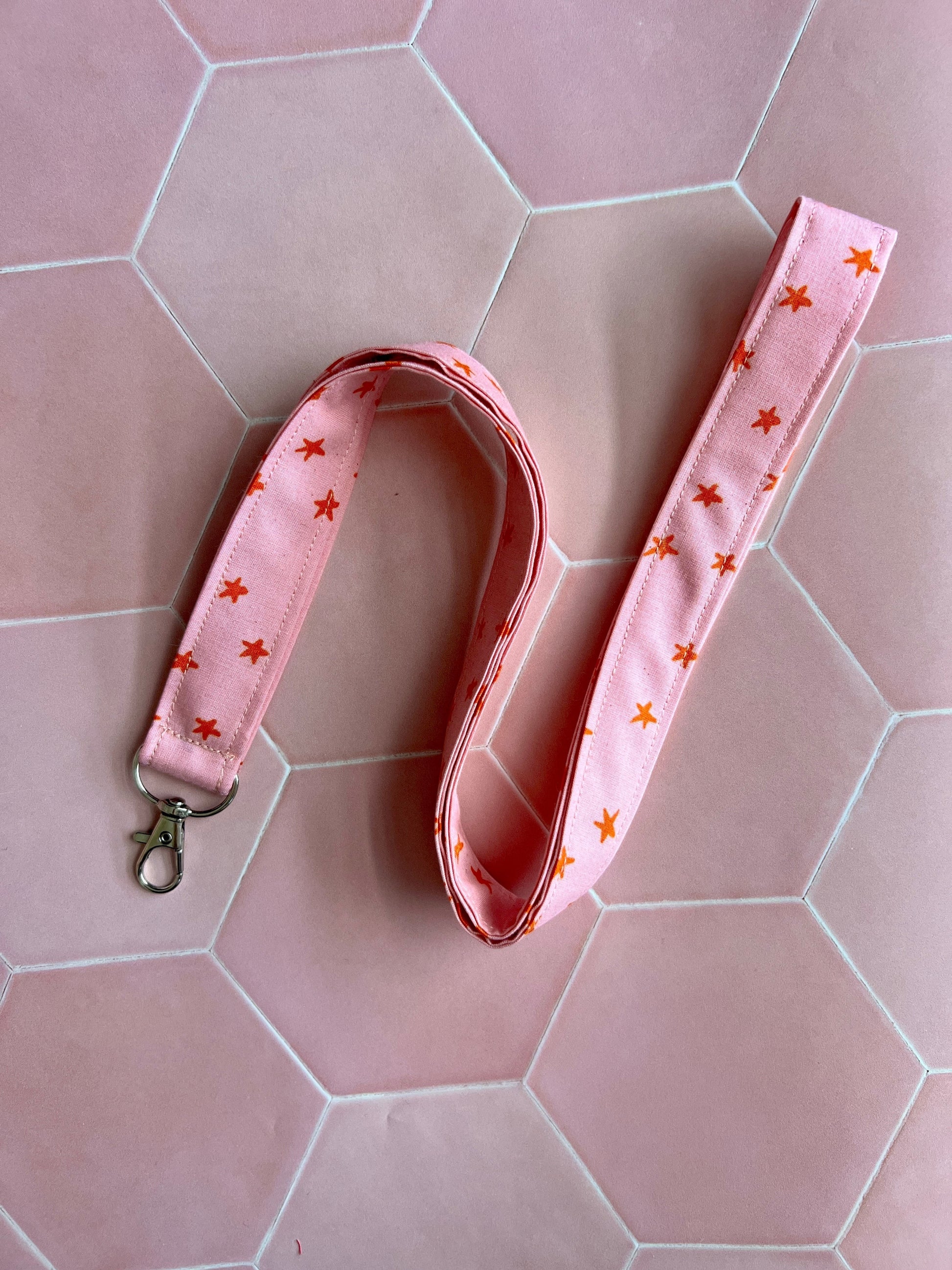 Sew Much Love pink fabric lanyard with orange stars and a silver D-ring clasp for keys or ID badges.