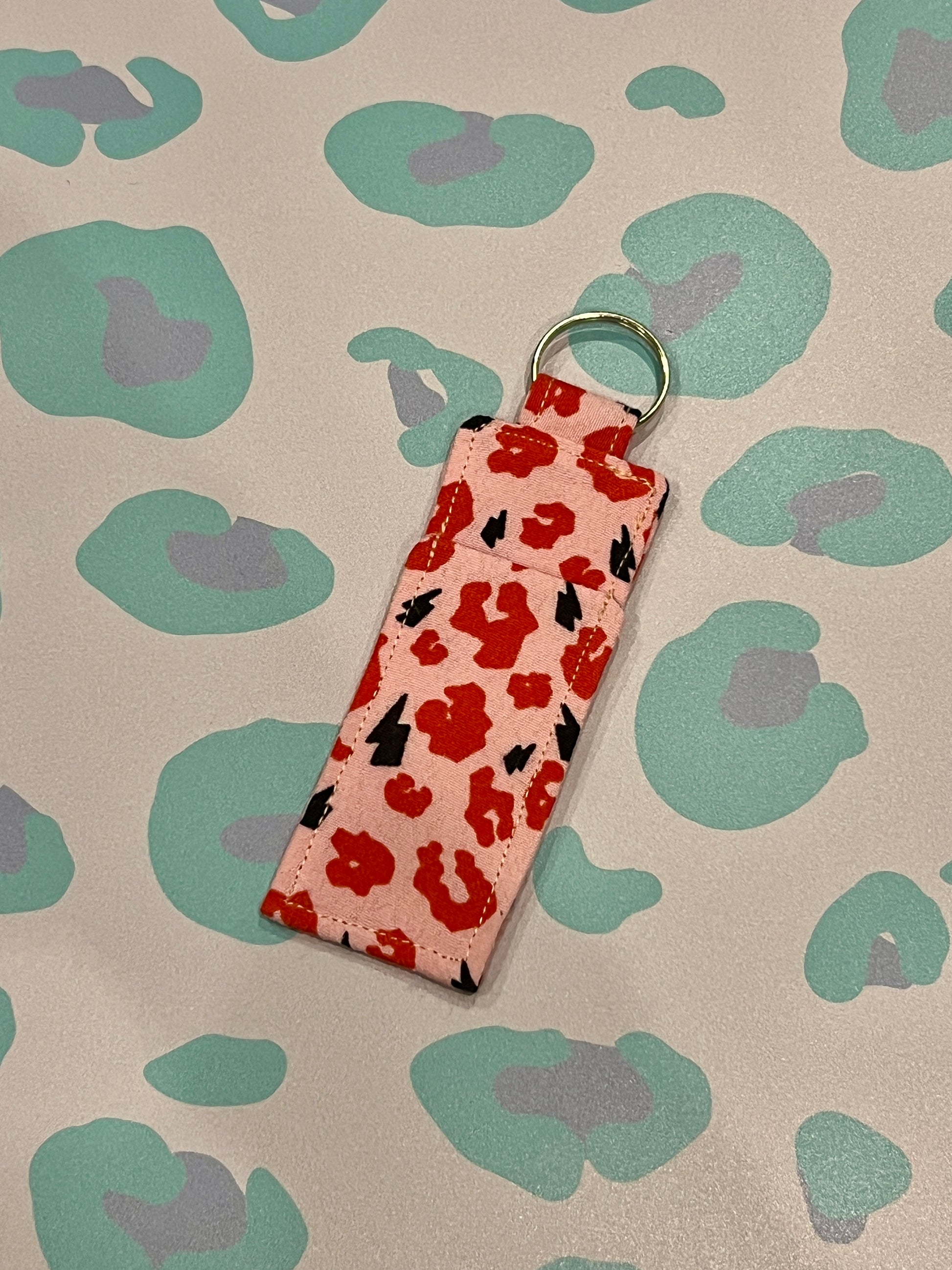 Rectangular key fob with red leopard print on a beige background with green and purple abstract shapes