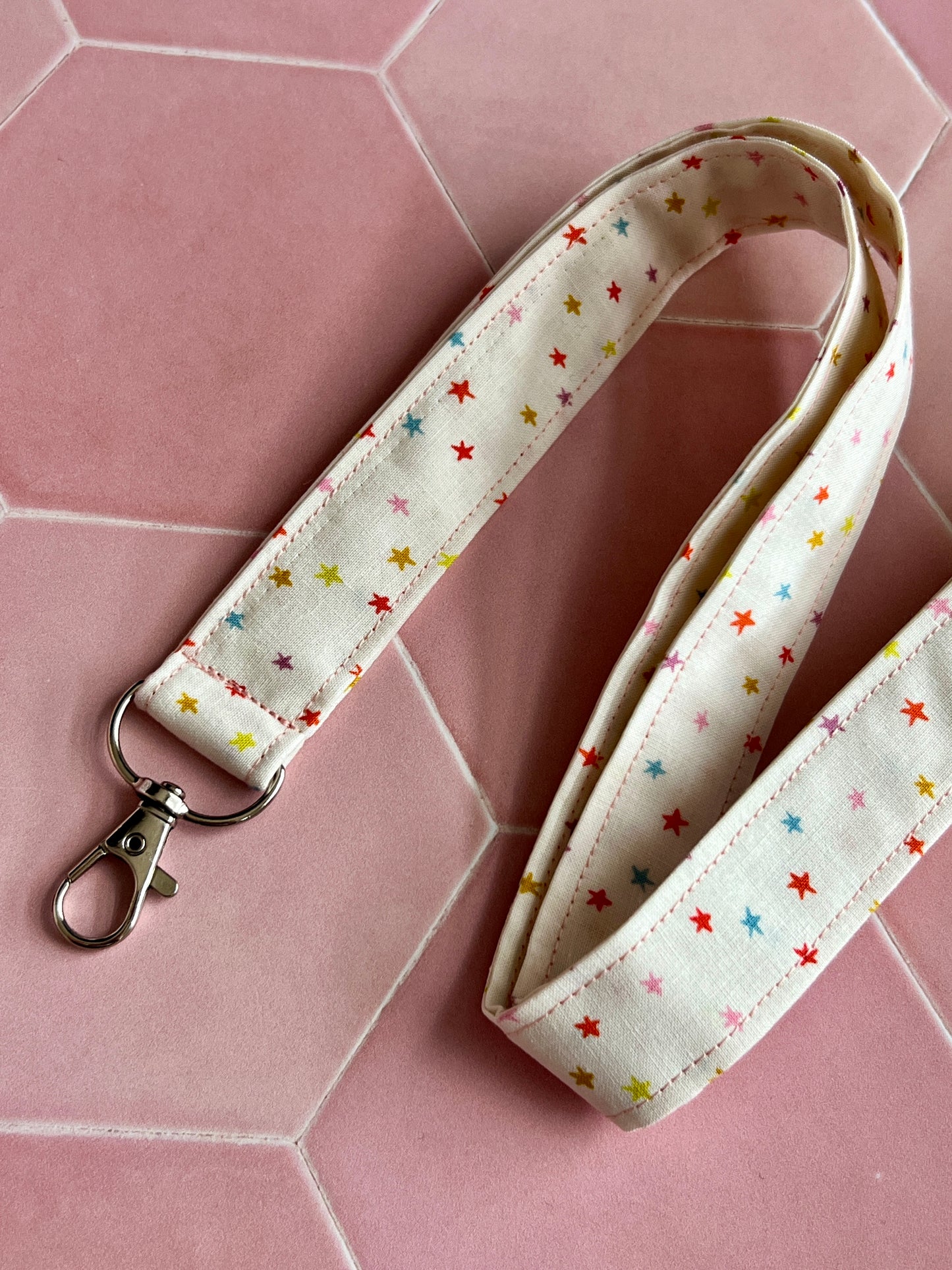Close-up of a handmade fabric lanyard with D-ring, featuring a cream background and rainbow mini star print, ideal for keys, ID badges, and small business accessories UK