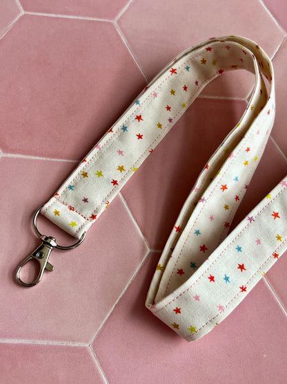 Close-up of a handmade fabric lanyard with D-ring, featuring a cream background and rainbow mini star print, ideal for keys, ID badges, and small business accessories UK