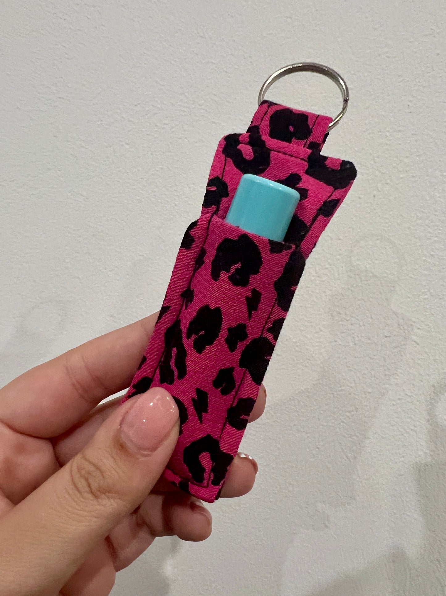 Pink leopard print keychain with a blue lip balm inside held by a hand against a light gray background.