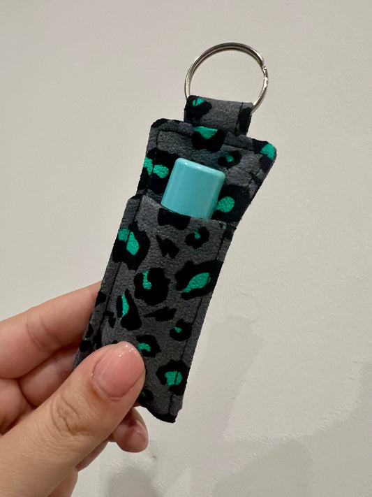 Keychain with leopard print pattern and lip balm held by a hand against a plain background