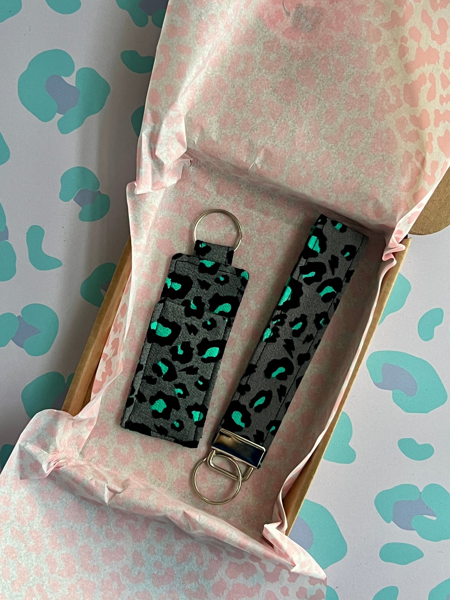 Sew Much Love handmade grey wristlet keychain with a black and teal snow leopard print. Features a metal clasp and keyring.