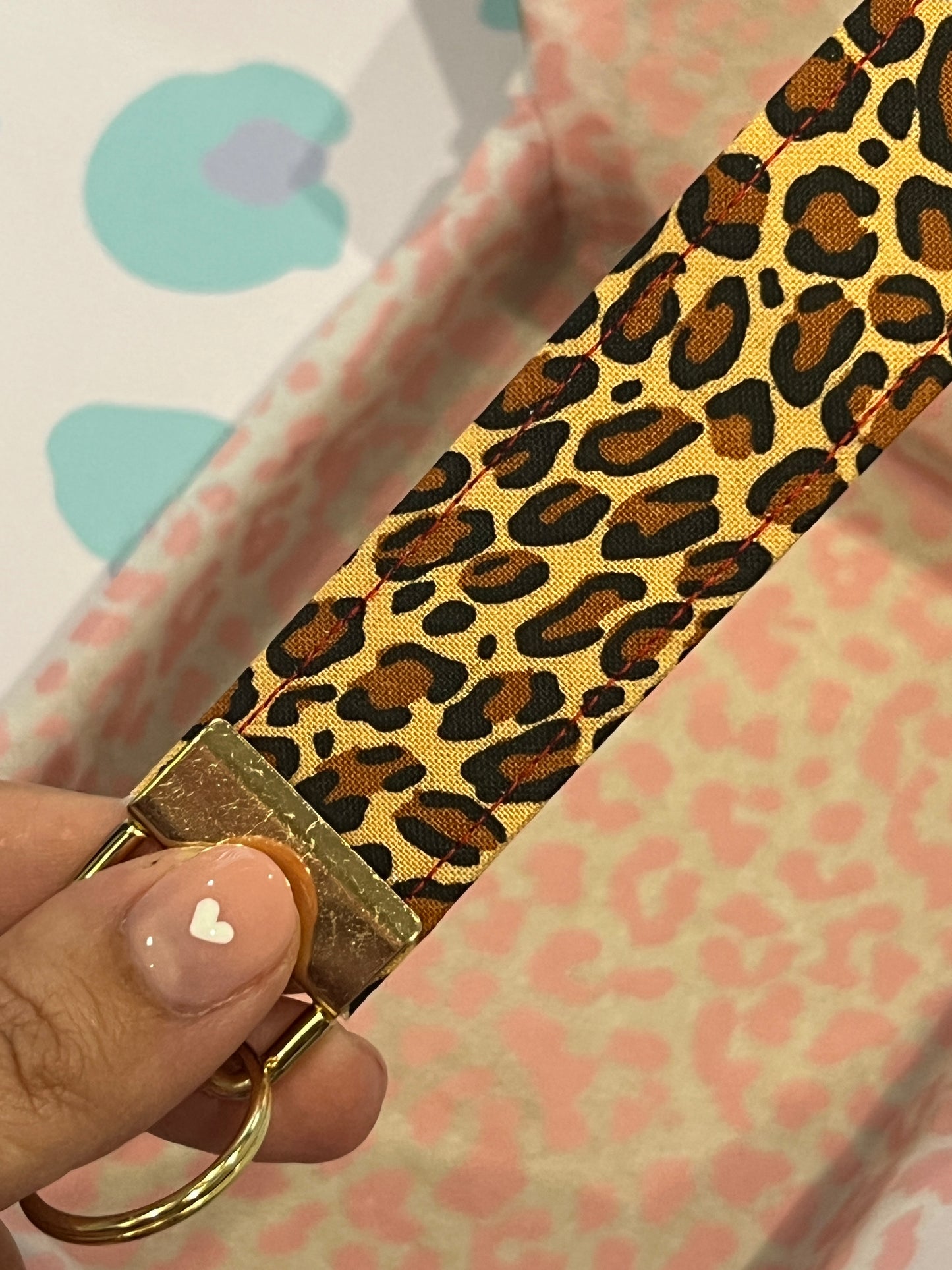 Leopard print keychain held by a hand with a pink background