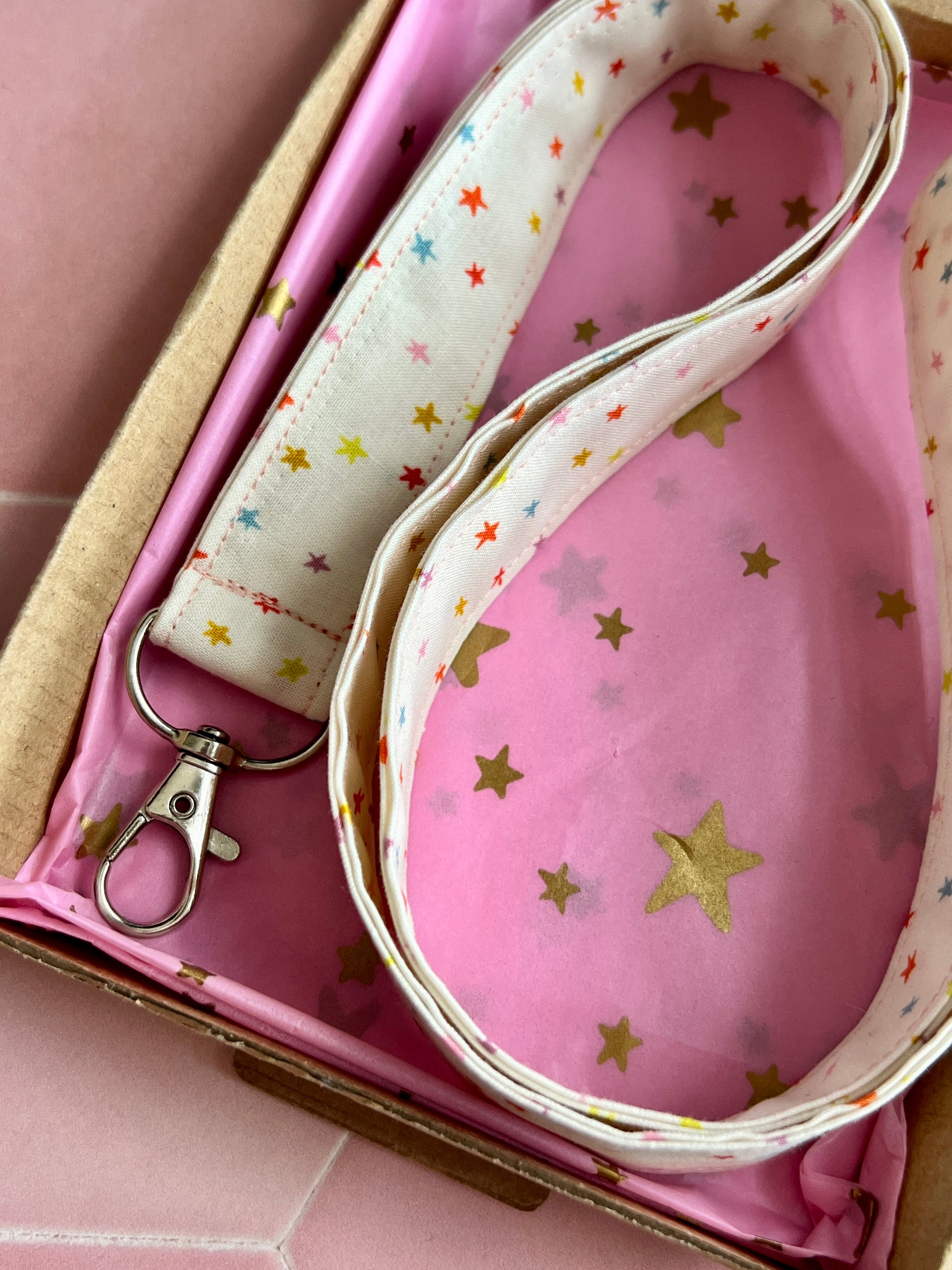 Fabric lanyard with rainbow star print, featuring a D-ring attachment, packaged in a gift box with pink and gold star tissue.
