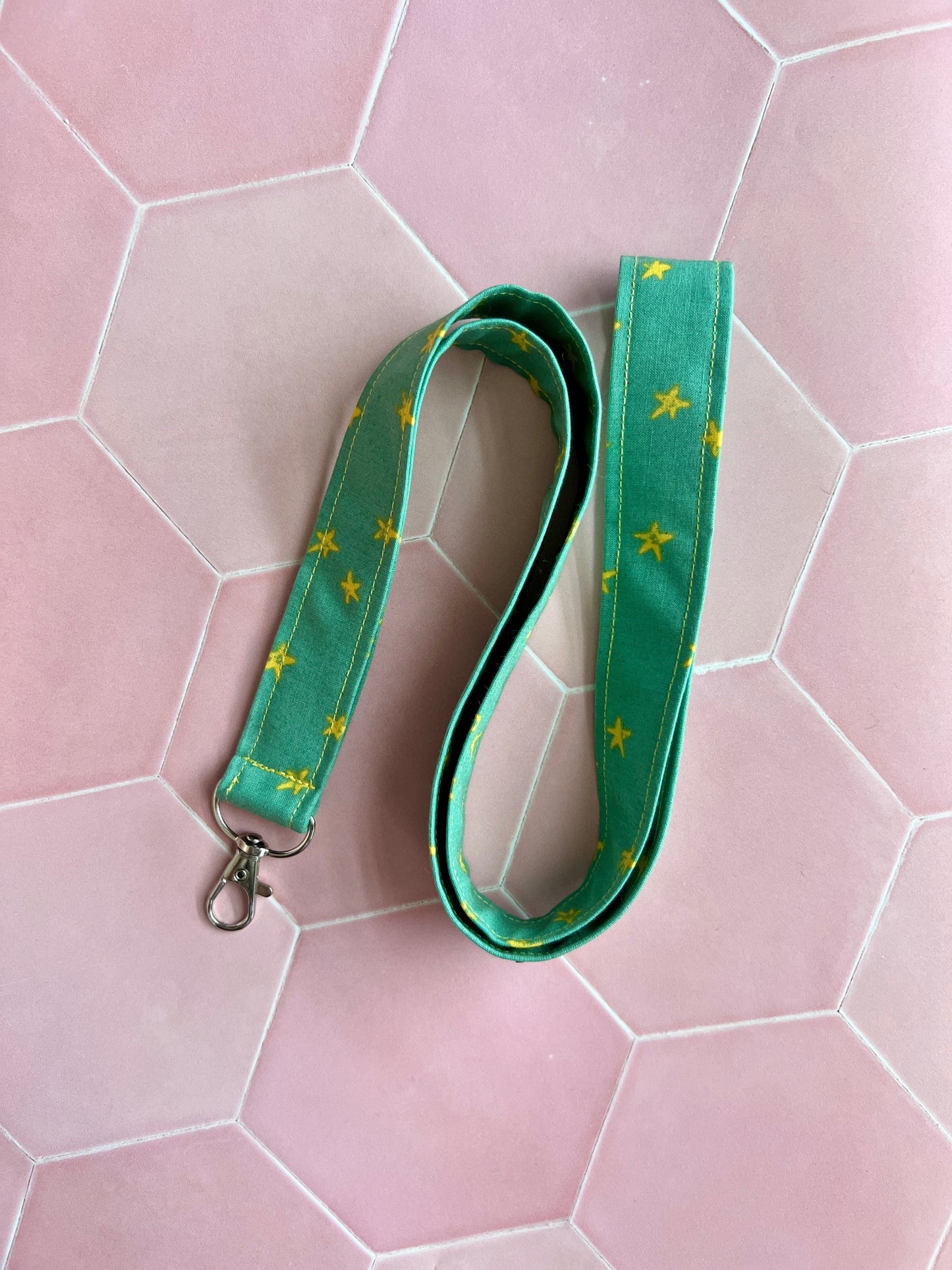 Sew Much Love green fabric lanyard with yellow stars and a metal D-ring clasp for keys or ID badges.