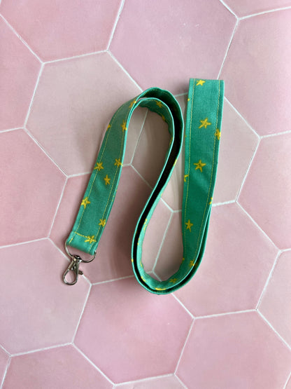 Sew Much Love green fabric lanyard with yellow stars and a metal D-ring clasp for keys or ID badges.