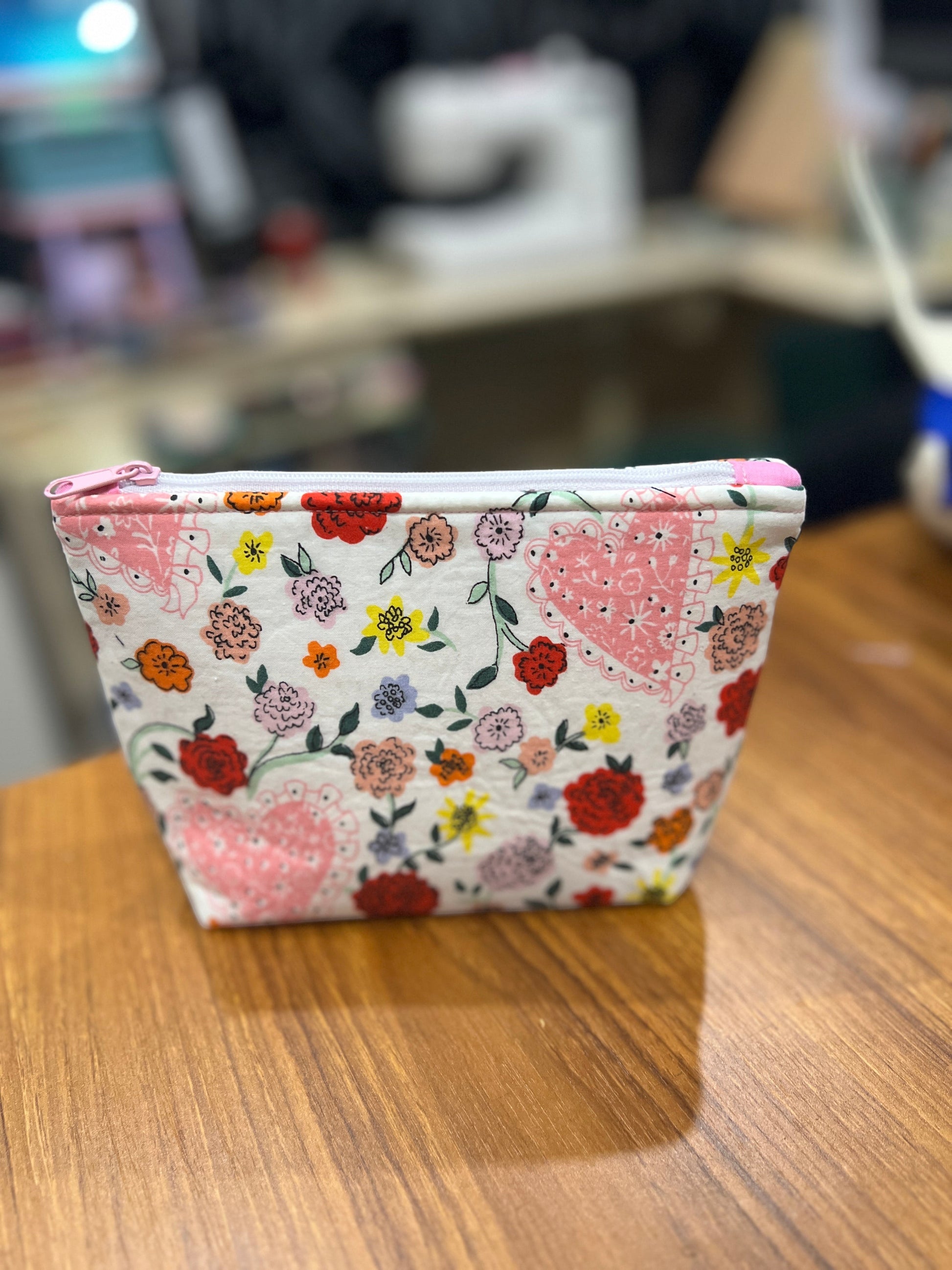 Sew Much Love mini cosmetic bag with white background, pink hearts, and multicoloured floral print. Features pink lining and white zip.