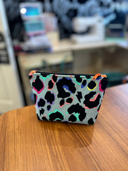 Sew Much Love mini cosmetic bag with grey background, black leopard print outlined in rainbow colours, and a orange zipper.