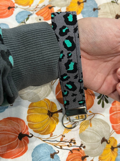 Sew Much Love grey wristlet keychain with black and teal snow leopard print. Features a metal D-ring and clasp.