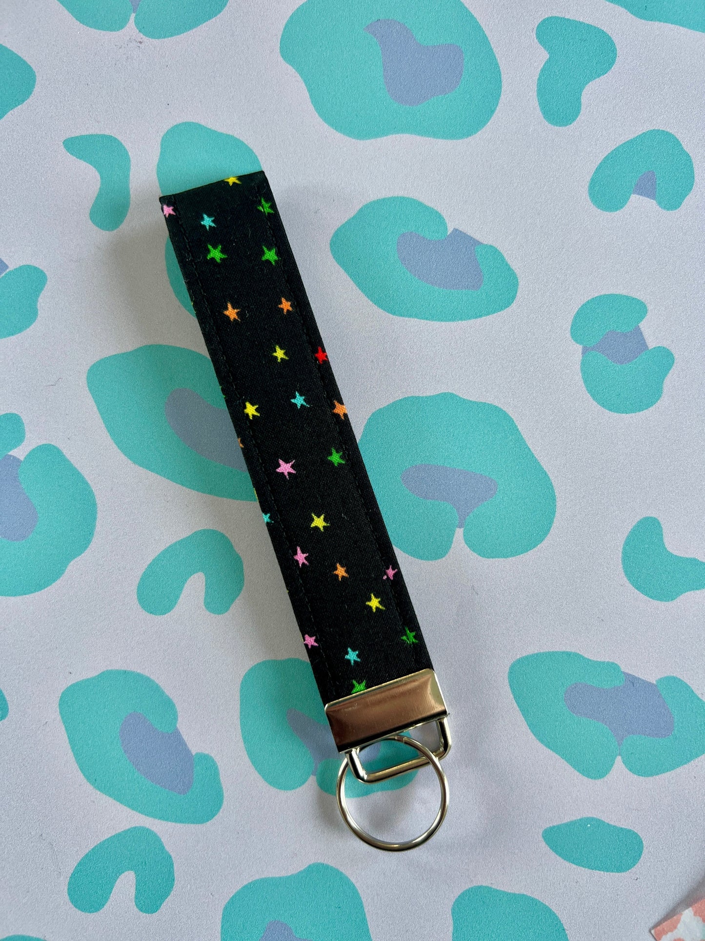 Sew Much Love black fabric wristlet keychain with small, colourful rainbow stars and silver hardware.